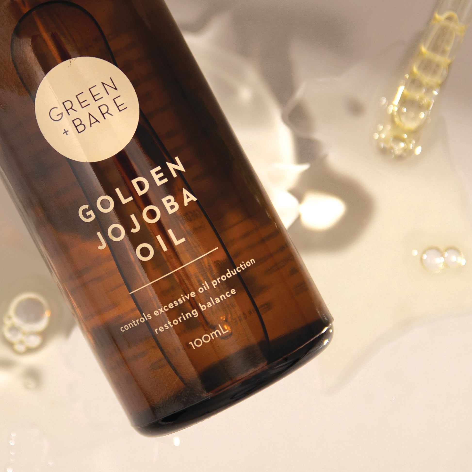Close up Golden Jojoba Oil Brown Bottle with transparent Jojoba oil in background